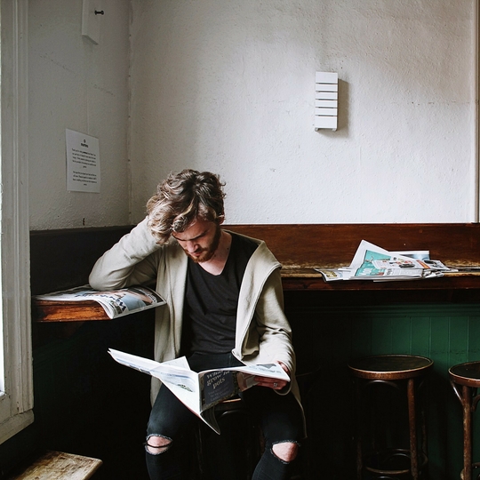 Man sitting on stool reading newspaper